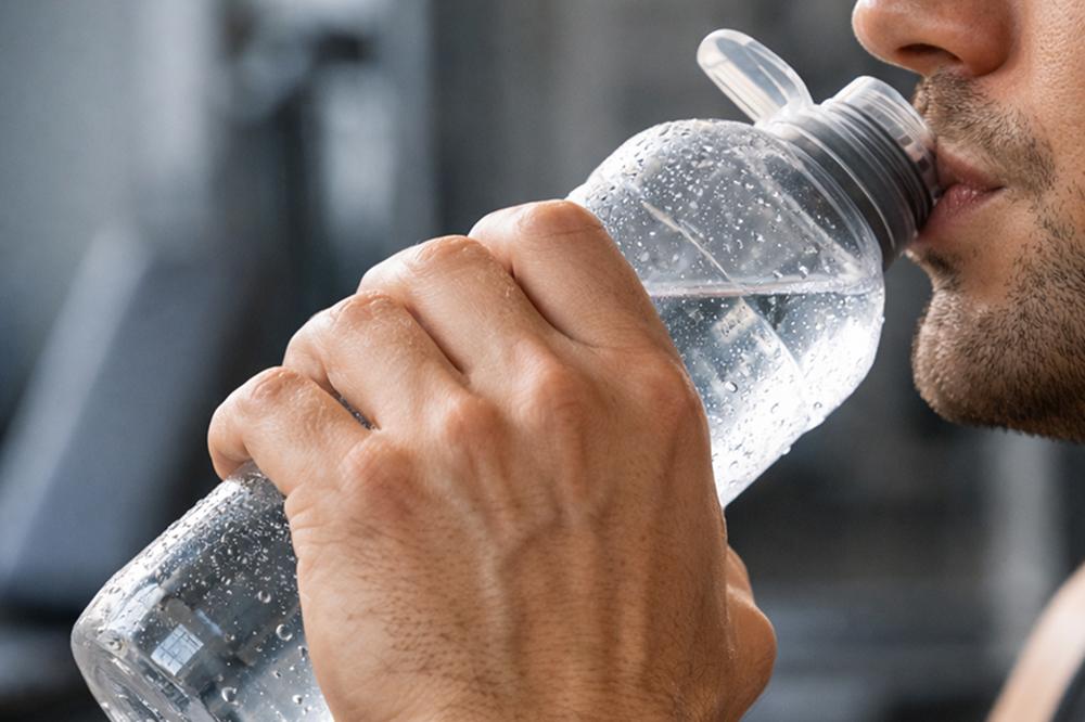 Спортсмен делает небольшой глоток воды во время паузы на тренировке в зале