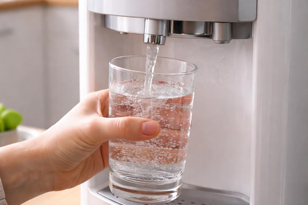 Чистая бутилированная вода наливается в стакан из кулера